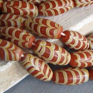 Può includere: Una collana di perline di vetro rosse e bianche con un motivo a spirale. Le perline sono di forma ovale e hanno una finitura lucida.