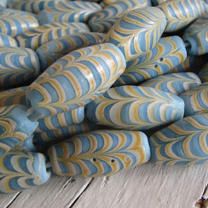 Può includere: Una collezione di perline di vetro a strisce blu e bianche. Le perline sono di forma ovale e hanno un motivo marmoreo.