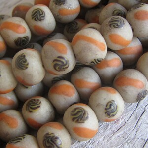 May include: A strand of white glass beads with orange and brown swirl designs. The beads are round and have a matte finish.