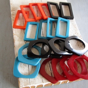 Può includere: Una collezione di componenti per gioielli in resina colorata, nei colori arancione, nero, blu e rosso. Le forme includono cornici rettangolari e quadrate, ideali per la creazione di orecchini, pendenti o altri accessori.