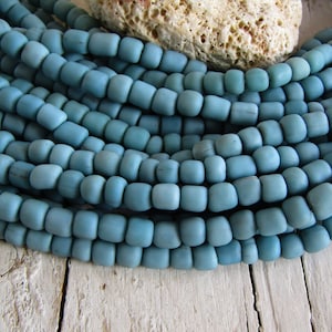 Può includere: Primo piano di una collana di perline di vetro blu chiaro. Le perline sono rotonde e hanno una finitura opaca. Le perline sono disposte in fila e impilate l'una sull'altra.
