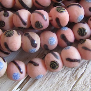 Op de afbeelding: Een streng roze glazen kralen met zwarte en blauwe swirl-ontwerpen. De kralen zijn rond en hebben een matte afwerking.