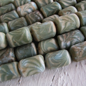 Puede incluir: Primer plano de cuentas rectangulares con un patrón veteado. Las cuentas presentan tonos verdes, crema y marrón, creando una estética natural. Ideales para la creación de joyas.