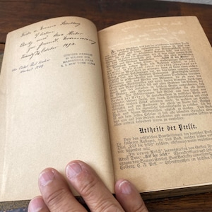 May include: An open antique book with cream-colored pages featuring German text. The left page displays handwritten cursive ink inscriptions and a printed address stamp for Gunther Haedich in New York. The right page contains printed paragraphs.