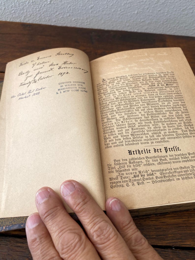 May include: An open antique book with cream-colored pages featuring German text. The left page displays handwritten cursive ink inscriptions and a printed address stamp for Gunther Haedich in New York. The right page contains printed paragraphs.