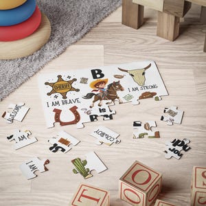 May include: A children's puzzle with a cowboy theme. The puzzle features a cowboy riding a horse, a sheriff's badge, and the text "I AM BRAVE". Additional puzzle pieces and wooden blocks with letters are scattered around.