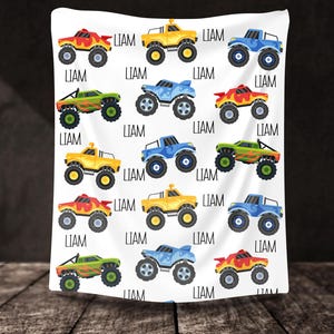 May include: A white background with a repeating pattern of monster trucks in blue, yellow, and green. The trucks have flames and are personalized with the name "LIAM".