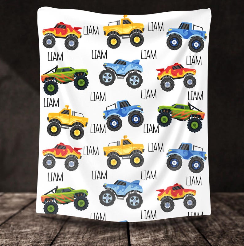 May include: A white background with a repeating pattern of monster trucks in blue, yellow, and green. The trucks have flames and are personalized with the name "LIAM".