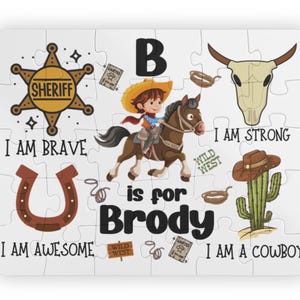 May include: A white jigsaw puzzle with a cowboy theme. The puzzle features a sheriff's badge, a horseshoe, a steer skull, and a cactus. Text includes "I AM BRAVE", "I AM AWESOME", "I AM STRONG", and "I AM A COWBOY". The name "Brody" is also featured.