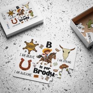 May include: A white jigsaw puzzle with a cowboy theme. The puzzle shows a cowboy on a horse, a sheriff's badge, a horseshoe, and the text "I am brave", "I am awesome", and "I am strong". The puzzle is personalised with the name "Brody".