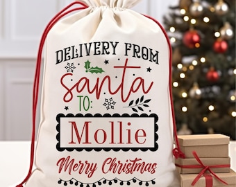 May include: White canvas Santa sack with red drawstring, featuring the text "Delivery from Santa to: Mollie Merry Christmas" in black and red lettering with a holly sprig and snowflakes.