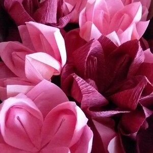 May include: A collection of pink and burgundy paper flowers. The flowers are made of crinkled tissue paper and have a delicate, feminine look.