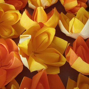May include: A close-up of a group of origami flowers in shades of orange and yellow. The flowers are made of paper and have a delicate, folded appearance.
