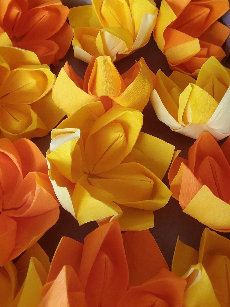 May include: A close-up of a group of origami flowers in shades of orange and yellow. The flowers are made of paper and have a delicate, folded appearance.