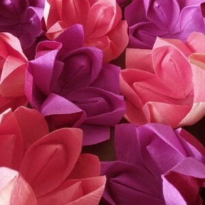 May include: A collection of origami flowers in shades of pink and purple. The flowers are made of paper and have a delicate, folded appearance.