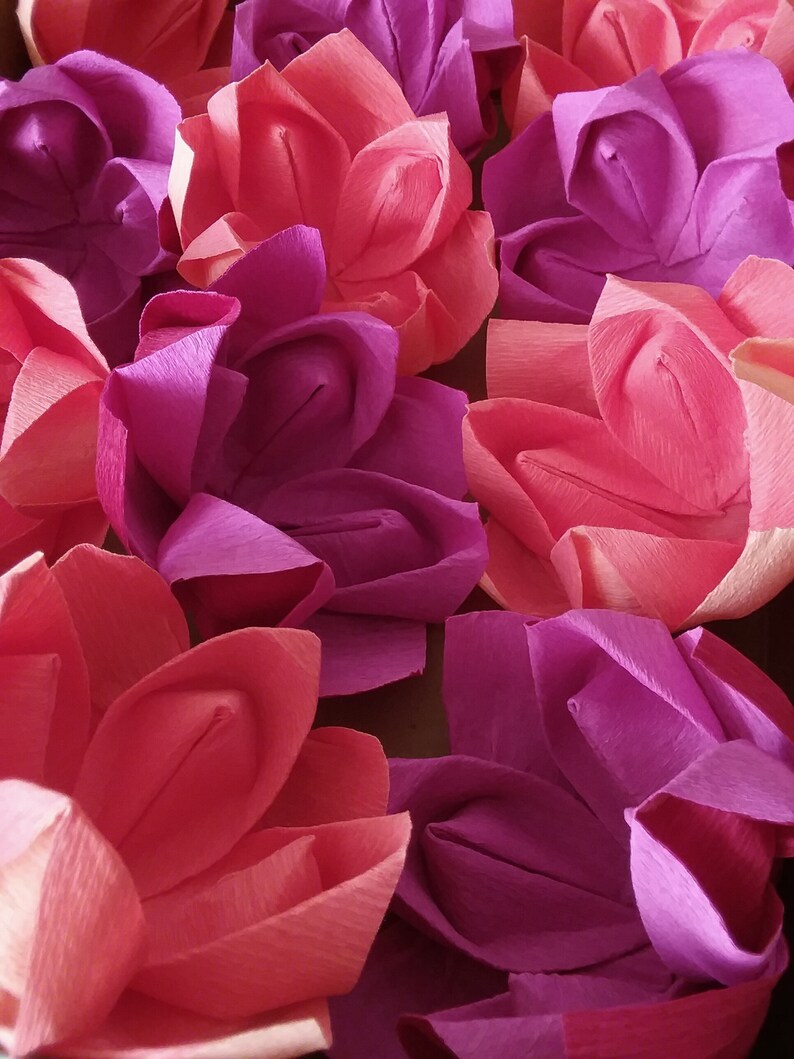May include: A collection of origami flowers in shades of pink and purple. The flowers are made of paper and have a delicate, folded appearance.