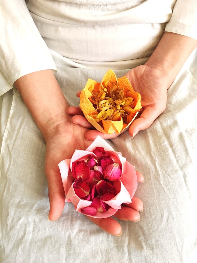 May include: Two paper flower arrangements, one yellow and one pink, are held in the hands of a person. The yellow flower is made of dried petals and the pink flower is made of dried rose petals.