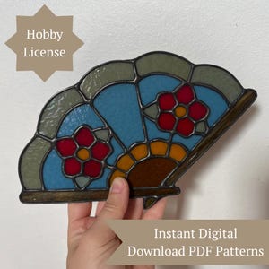 Op de afbeelding: Een waaiervormig paneel van glas-in-lood met blauwe, groene, rode en gele glassegmenten verbonden door donkere metalen soldeerlijnen. Het ontwerp bevat twee rode bloemen met gele harten. De tekst op de afbeelding luidt Hobby License en Instant Digital Download PDF Patterns.