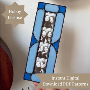 May include: A rectangular stained glass photo frame featuring light and dark blue glass panels joined by dark metal solder lines. The centre holds a vertical strip of four black and white photo booth pictures with the text THE SHORT STOP.