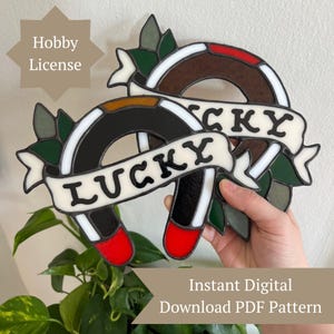 Puede incluir: Dos diseños de herraduras de vidrieras con la palabra "LUCKY" en una pancarta. Las herraduras son negras, marrones y blancas con detalles en rojo. La imagen también incluye el texto "Hobby License" y "Instant Digital Download PDF Pattern".