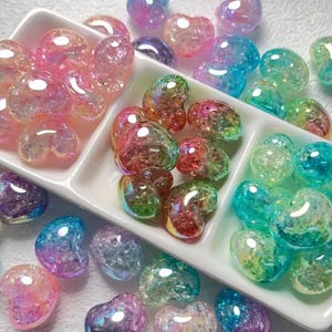 May include: Assortment of iridescent heart-shaped glass beads in pink, green, and blue colors. The beads are arranged in three sections of a white divided dish.