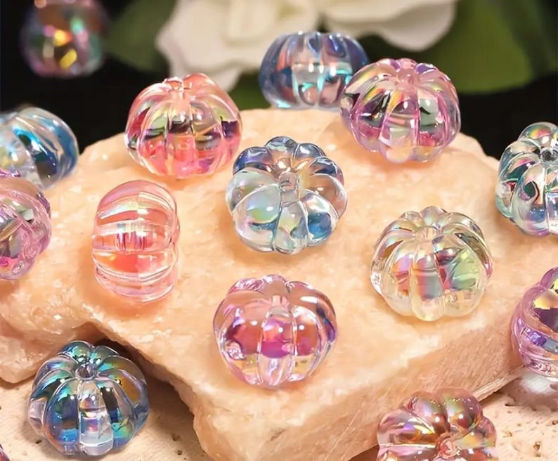 May include: A collection of iridescent glass pumpkin beads in various shades of pink, blue, and purple. The beads have a textured surface and are perfect for crafting.
