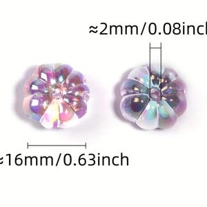 May include: Two iridescent purple pumpkin-shaped beads with a hole in the center. The beads are approximately 0.63 inches wide and 0.08 inches thick.