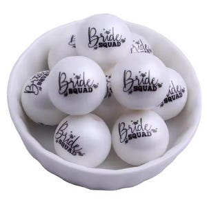Peut inclure: Boules en plastique blanches avec le texte "Bride Squad" imprimé en noir. Les boules sont dans un bol blanc.