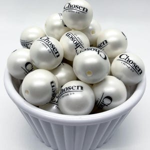 May include: A white bowl filled with round, pearl-like beads. Each bead has a smooth, lustrous finish and is printed with the black text "Chosen" followed by "1 PETER 2:9". The beads feature a small hole for threading, and the bowl has a fluted edge.