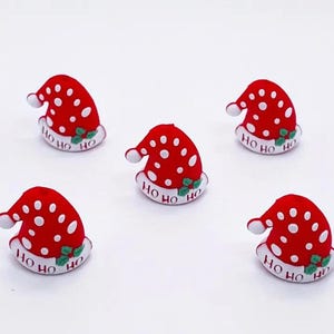 May include: Five red and white Christmas hat decorations with white polka dots and the words "Ho Ho Ho" written on them.