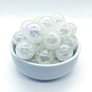 Peut inclure: Un bol blanc rempli de perles de verre irisées. Les perles sont rondes et ont une surface texturée.