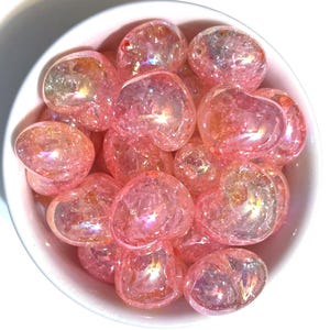 May include: A bowl filled with pink iridescent tumbled stones. The stones are smooth and have a sparkly, glittery appearance.