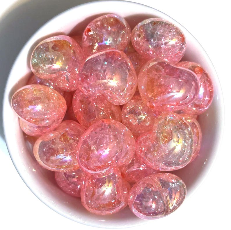 May include: A bowl filled with pink iridescent tumbled stones. The stones are smooth and have a sparkly, glittery appearance.