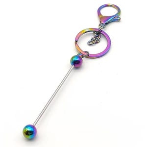 May include: A rainbow iridescent metal keychain with a long, thin metal rod and two round beads at the ends. The keychain has a metal ring and a lobster claw clasp.