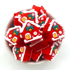 May include: A bowl filled with red, white, and green gingerbread house-shaped charms. The charms have white frosting, green bows, and gold bells.