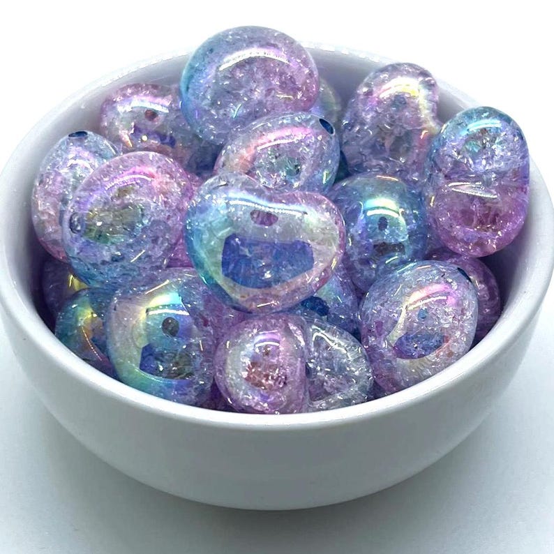 May include: A bowl filled with iridescent heart-shaped glass beads. The beads are a mix of light blue and pink with a glittery finish.