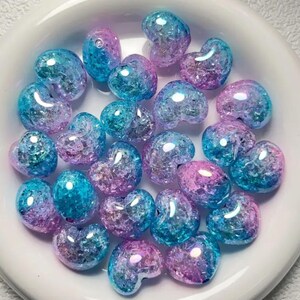 May include: A collection of heart-shaped glass beads in shades of blue and pink with a glittery finish.