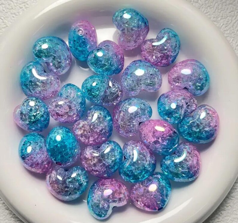 May include: A collection of heart-shaped glass beads in shades of blue and pink with a glittery finish.