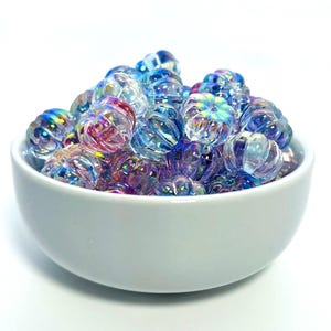 May include: A white ceramic bowl filled with iridescent glass beads. The beads are a mix of blue, purple, and pink.