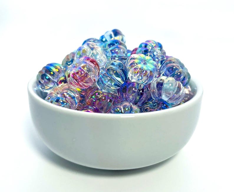 May include: A white ceramic bowl filled with iridescent glass beads. The beads are a mix of blue, purple, and pink.