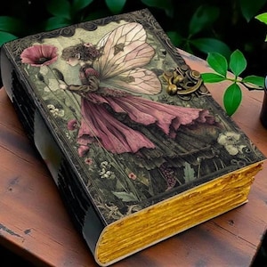 May include: A rectangular journal with a dark cover featuring a fairy illustration in a floral setting. The cover has a metallic latch closure and the page edges are finished in a bright gold colour, creating a distinct contrast against the dark cover.