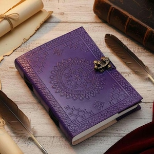 May include: A purple leather journal with an embossed floral design and a metal clasp. The journal is open, revealing blank pages. Decorative feathers and rolled parchment surround the journal, suggesting a vintage or fantasy theme.