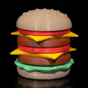 May include: A 3D printed model of a hamburger with a brown bun, yellow cheese, red tomato slices, green lettuce, and a brown patty.