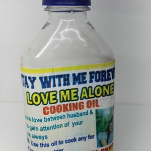 May include: A clear glass bottle with a blue cap and a yellow label that reads "Stay With Me Forever Love Me Alone Cooking Oil". The label also includes the text "Use this oil to cook any for your partner" and "Oluwa Spiritual Products".