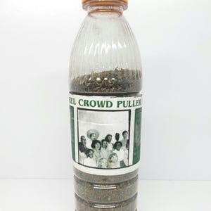 May include: A clear plastic bottle with a yellow lid filled with dried herbs. The bottle has a green label with the text "REL CROWD PULLER" and a black and white photo of a group of people.