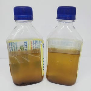 May include: Two clear plastic bottles with blue lids filled with a yellow liquid. The bottles have labels with the text "STAY IN LOVE" and "ERI-DLUVW".