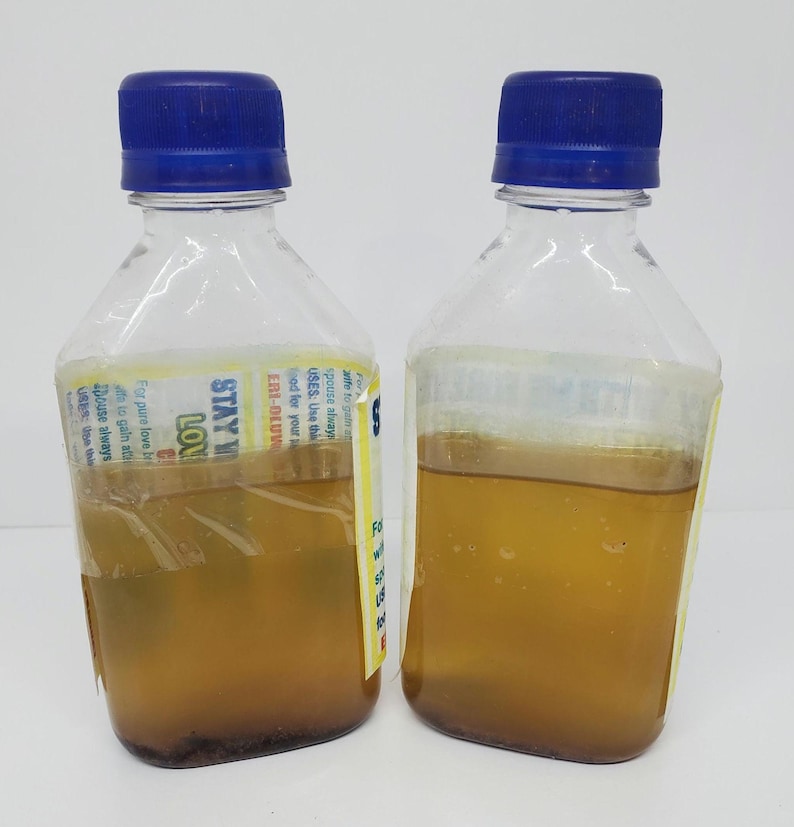 May include: Two clear plastic bottles with blue lids filled with a yellow liquid. The bottles have labels with the text "STAY IN LOVE" and "ERI-DLUVW".