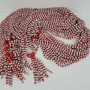 May include: A bundle of red and white beaded necklaces with red beads at the ends. The necklaces are made of small, round beads and are arranged in a circular pattern.