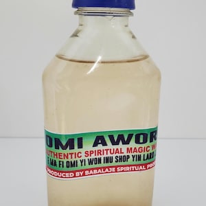 May include: A clear glass bottle with a blue cap, containing a light brown liquid. The bottle has a green and white label that reads "OMI AWOR AUTHENTIC SPIRITUAL MAGIC WATER NA FI OMI YI WON INU SHOP YIN LARD PRODUCED BY BABALAJE SPIRITUAL PRODUCTS."
