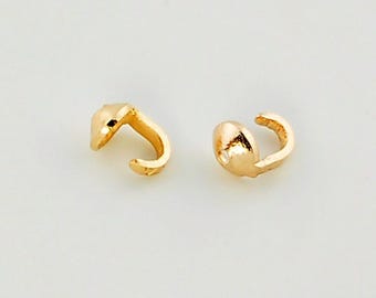 May include: Two gold-colored metal crimp covers, each featuring a small, rounded, dome-shaped top with a curved, open hook-like structure extending from the side, designed for securing jewelry findings and concealing knots in cord or wire.